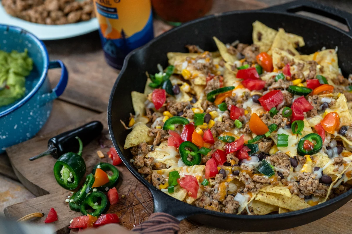 Loaded campfire nachos in a cast-iron skillet on an outdoor table