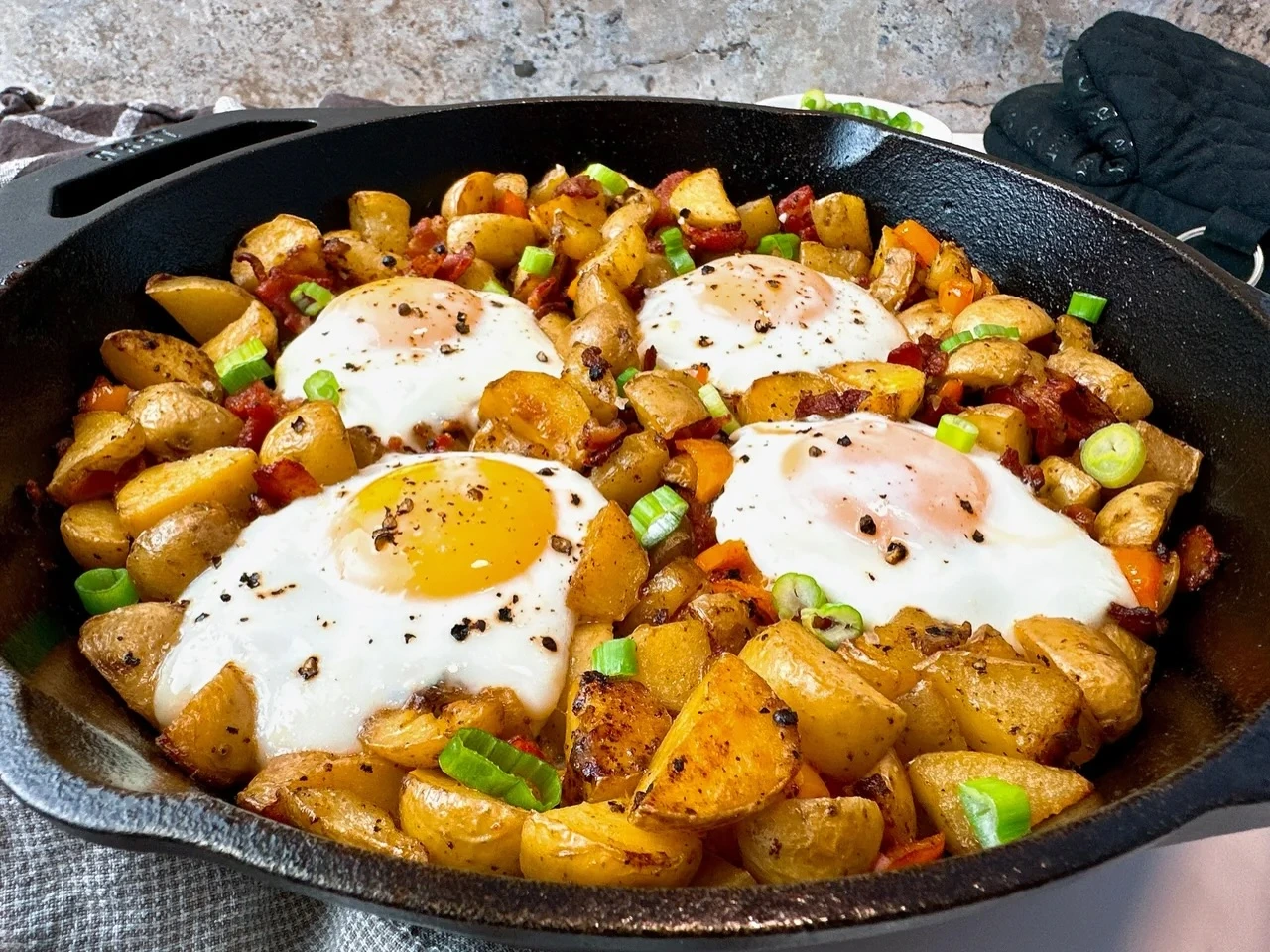 Skillet of potato and pepper hash topped with baked eggs