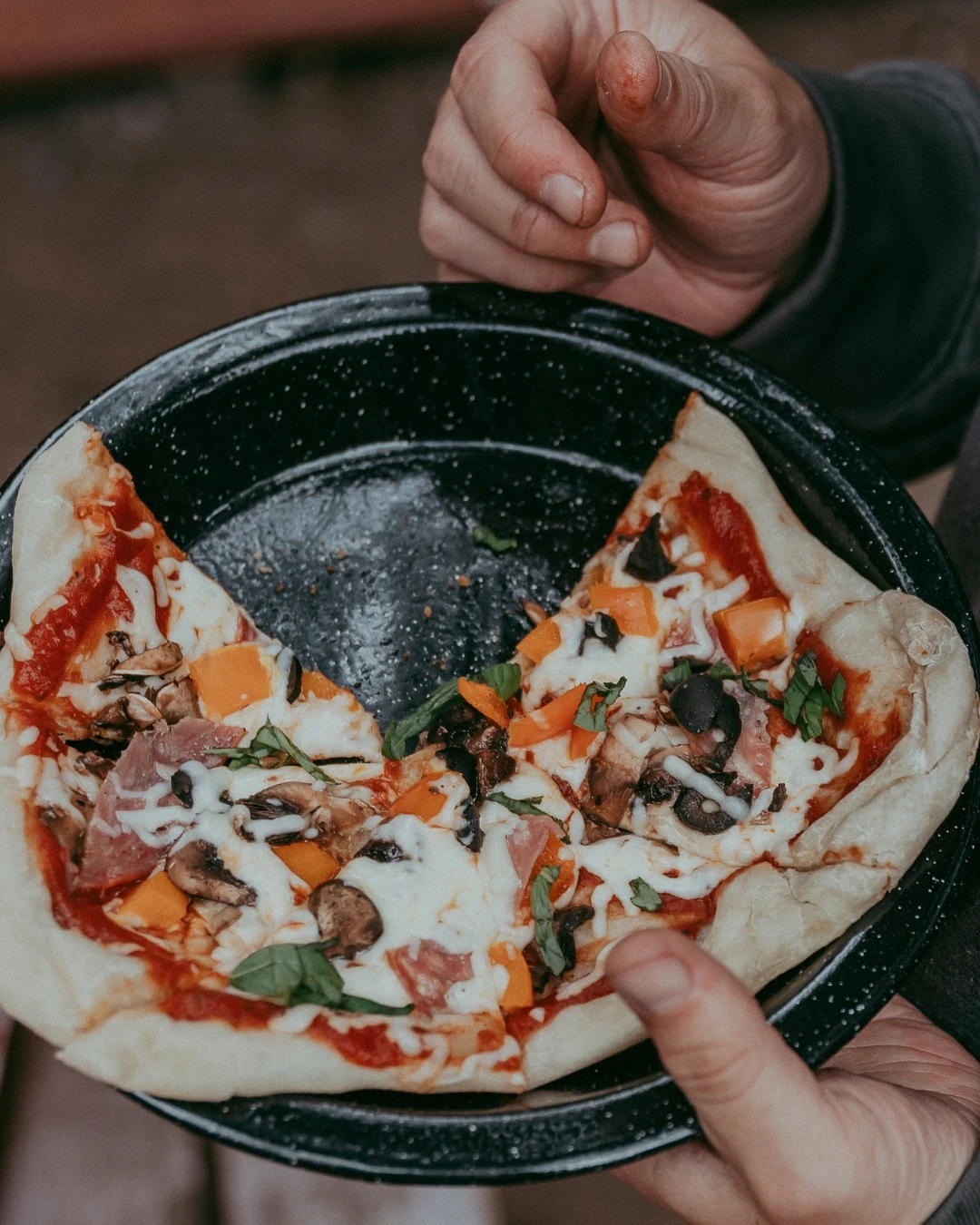 Slices of vegetable campfire pizza on a black camping plate