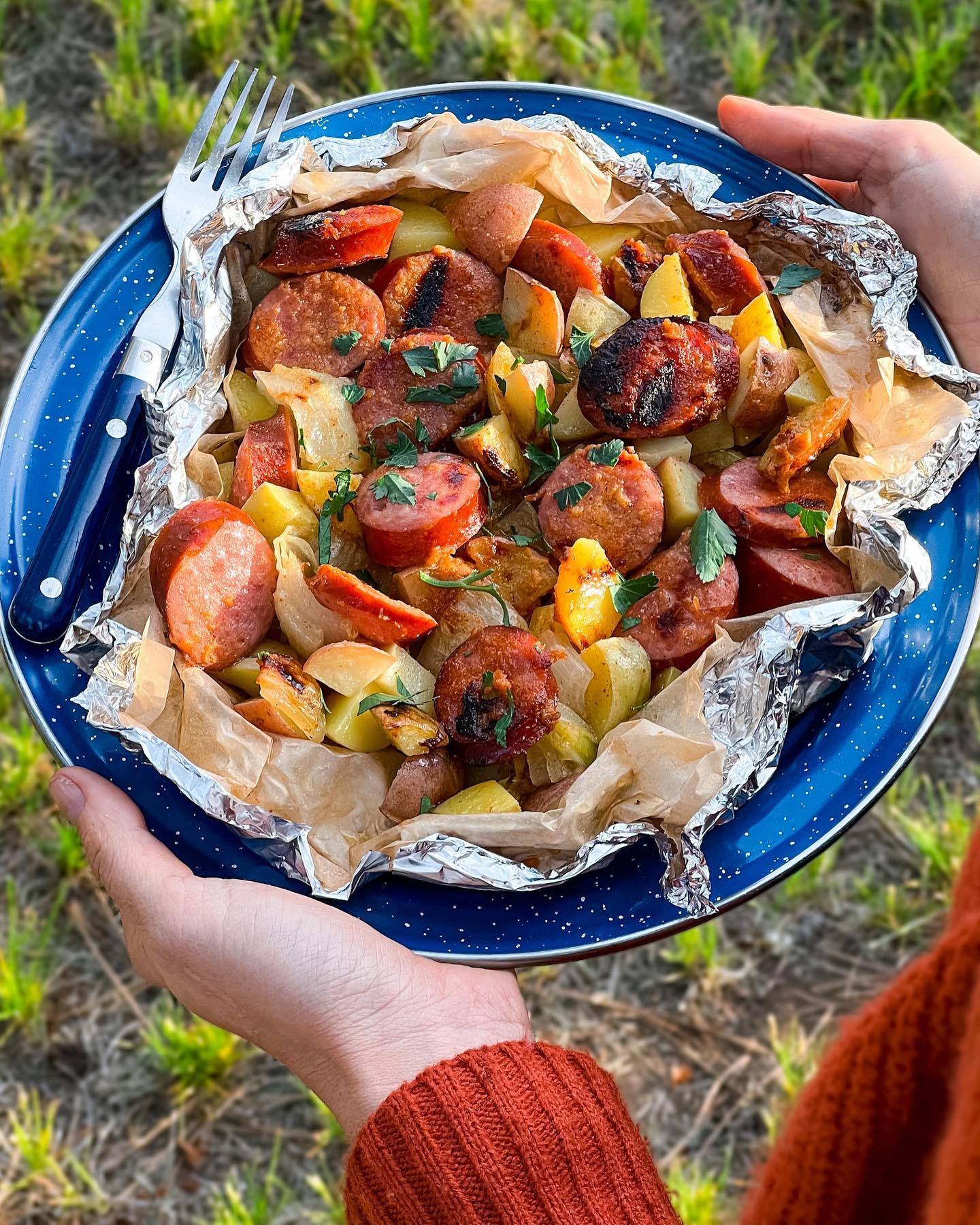 Sausage and potato foil-packet dinner on a blue camping plate