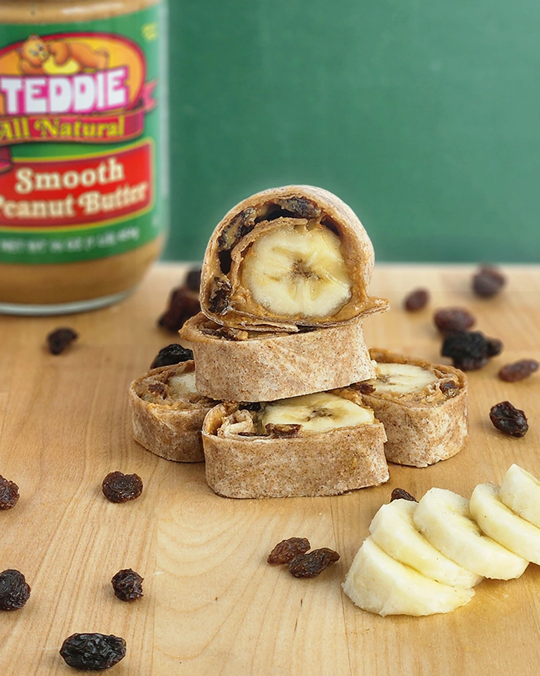 Peanut butter banana and raisin tortilla rolls stacked on a wooden board