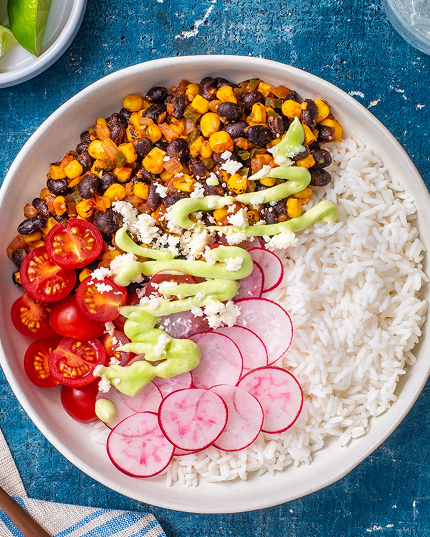 Rice bowl with black beans, corn, tomatoes, radishes and avocado crema