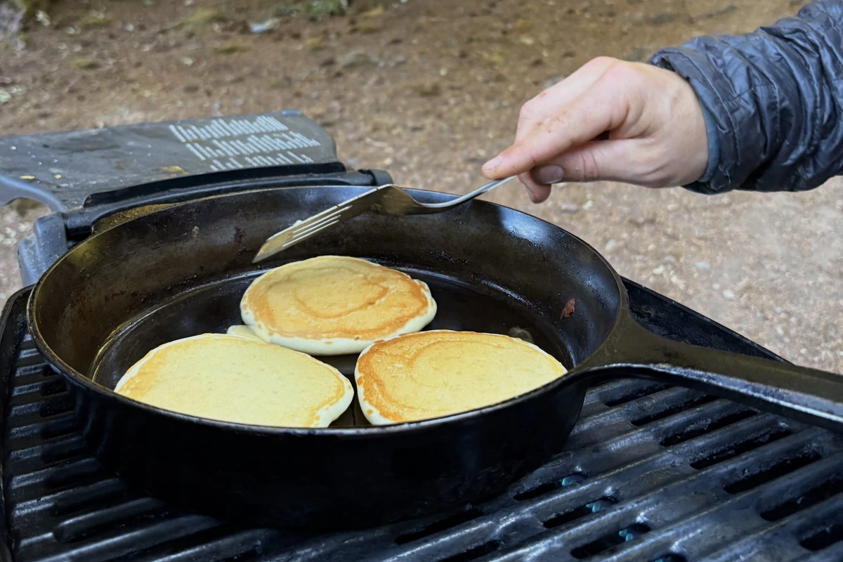 Pancakes cooking in a cast-iron skillet at a wooded campsite