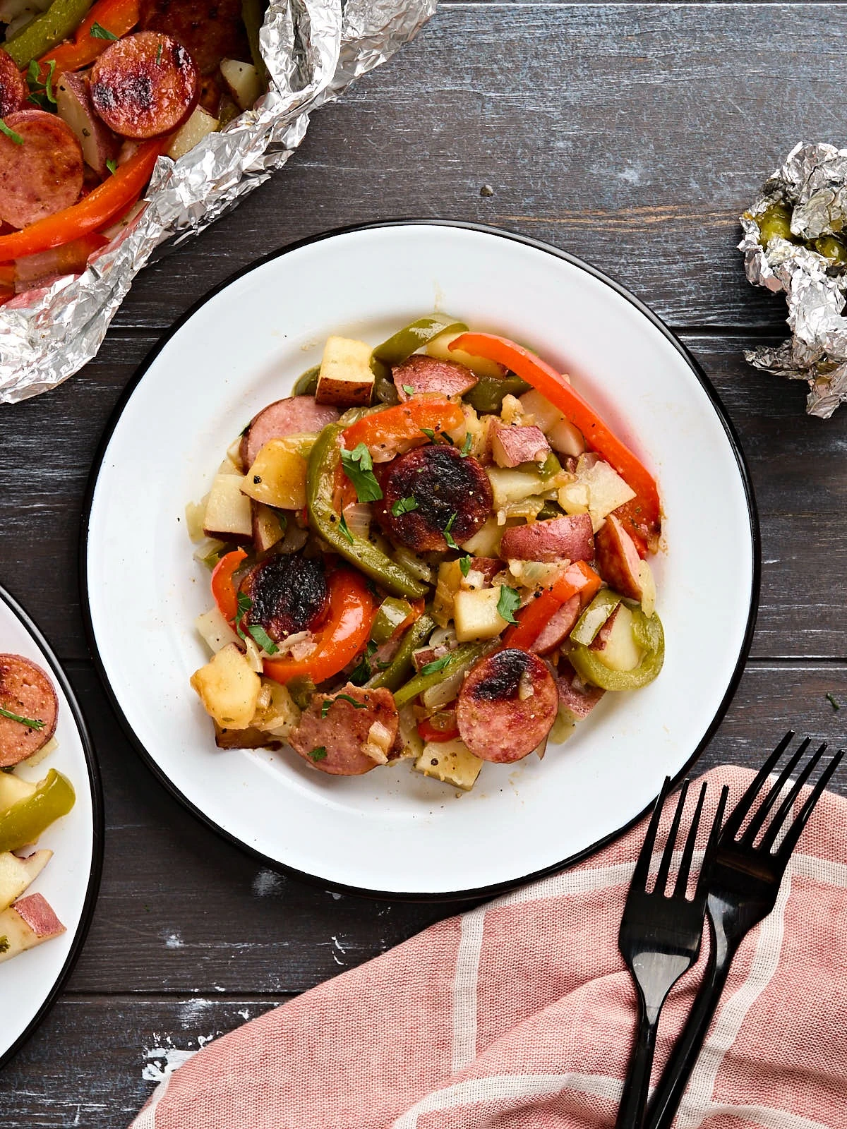 Grilled sausage, potatoes and peppers served beside opened foil packets