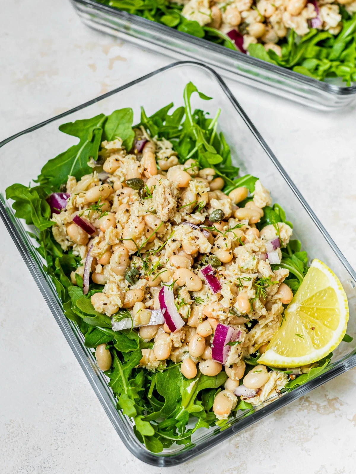 Tuna and white bean salad over leafy greens in a glass meal container