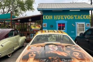 A decorated car parked outside the turquoise Con Huevos Tacos building in San Antonio