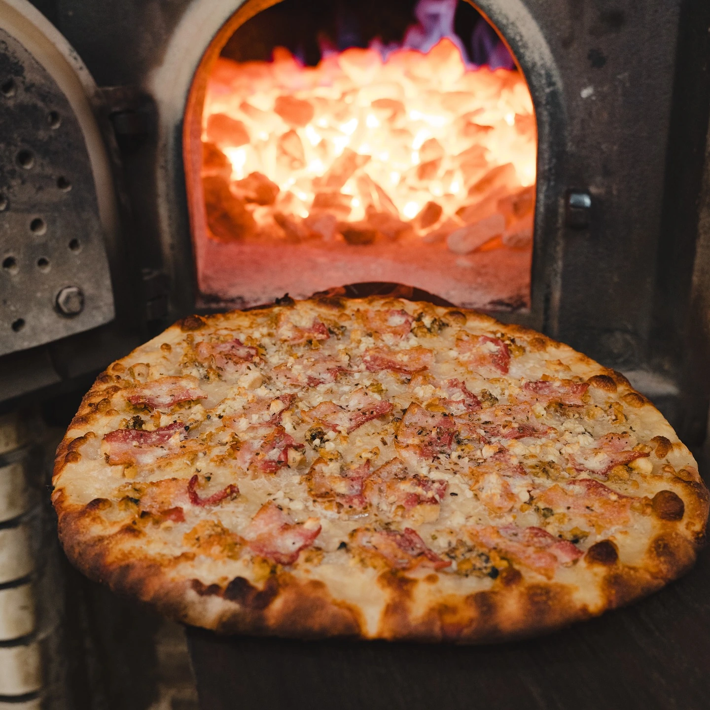 White clam pizza with bacon beside a coal-fired oven at Frank Pepe Pizzeria