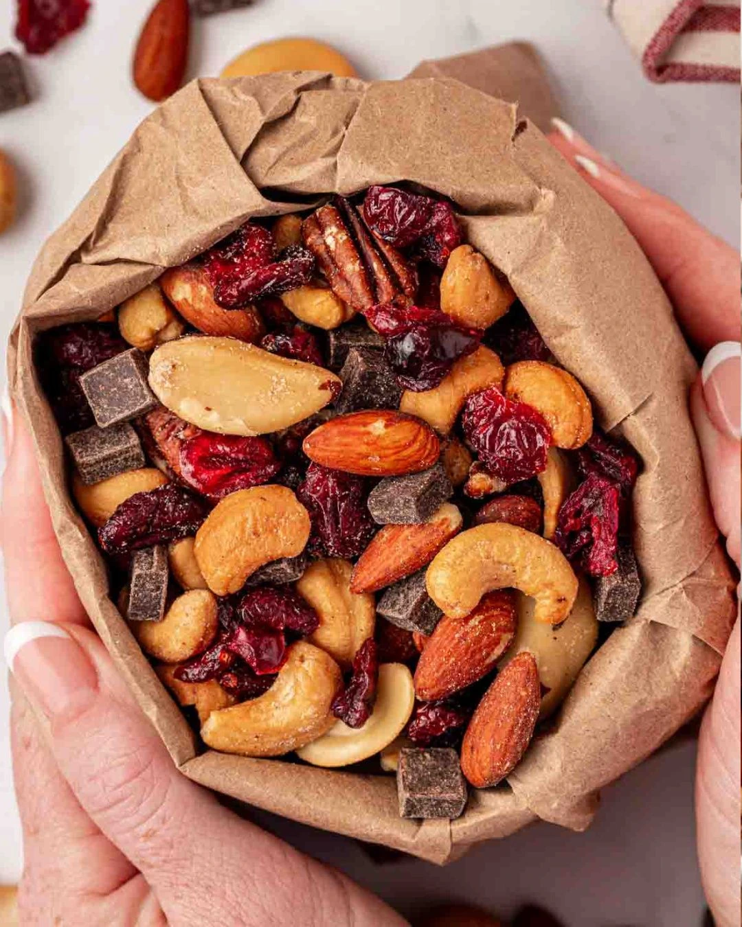 Paper bag of homemade trail mix with nuts, dried cranberries and dark chocolate