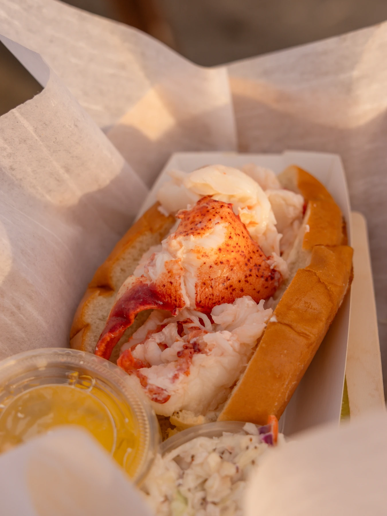 McLoons lobster roll with a cup of melted butter and coleslaw