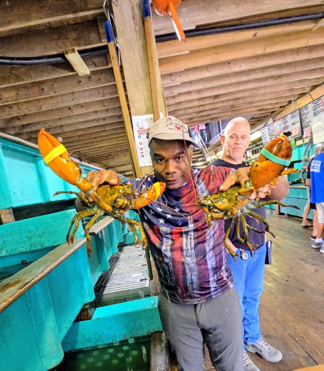 A visitor holding two live lobsters beside the tanks at Young’s Lobster Pound in Belfast