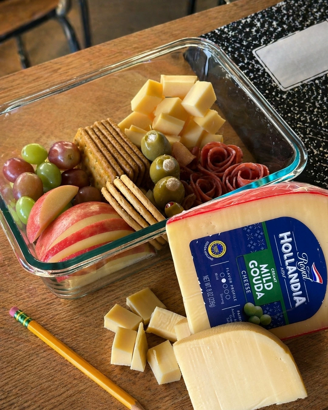 Glass snack box with apple slices, cheese cubes, crackers, grapes and olives