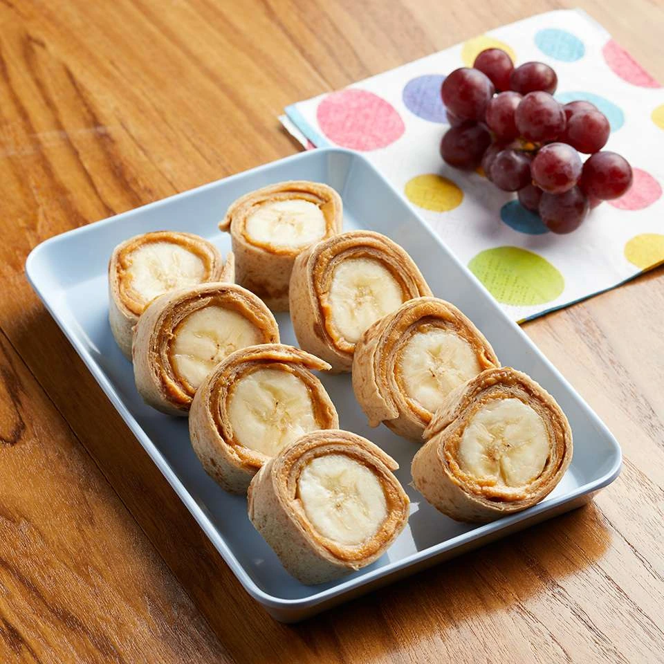 Peanut butter banana tortilla rolls arranged on a blue plate beside grapes