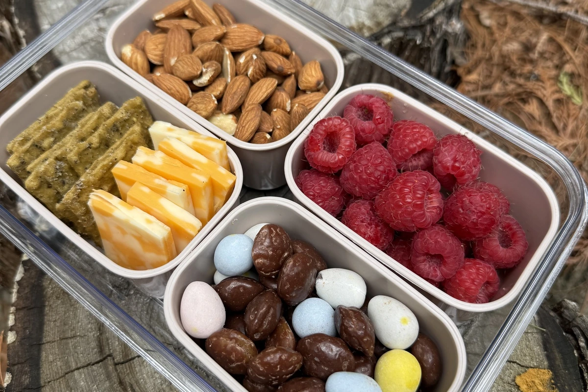 Outdoor snack box with raspberries, almonds, cheese, crackers and sweet treats on a tree stump