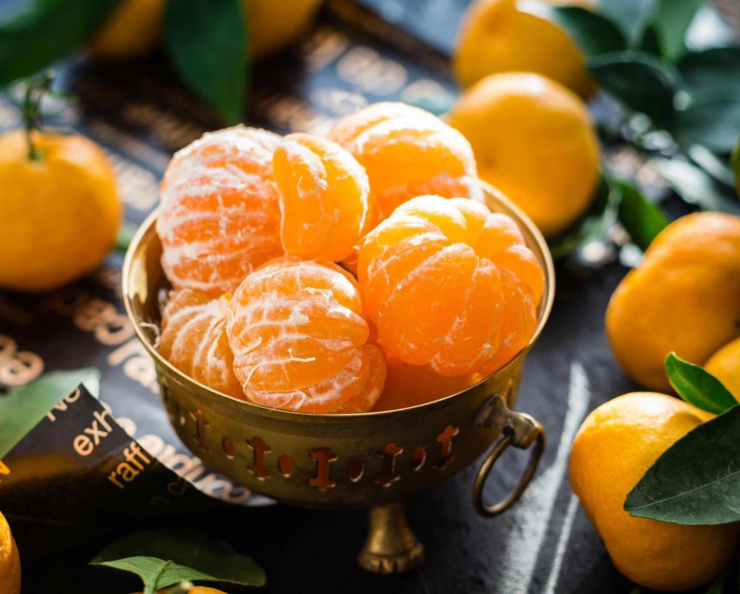 Peeled clementines in a serving bowl with whole citrus fruit nearby