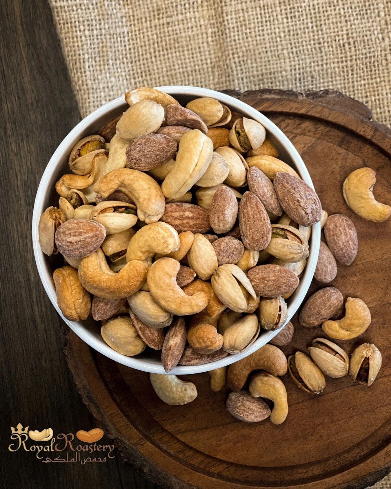 Mixed almonds, cashews and pistachios in a white bowl on a wooden board