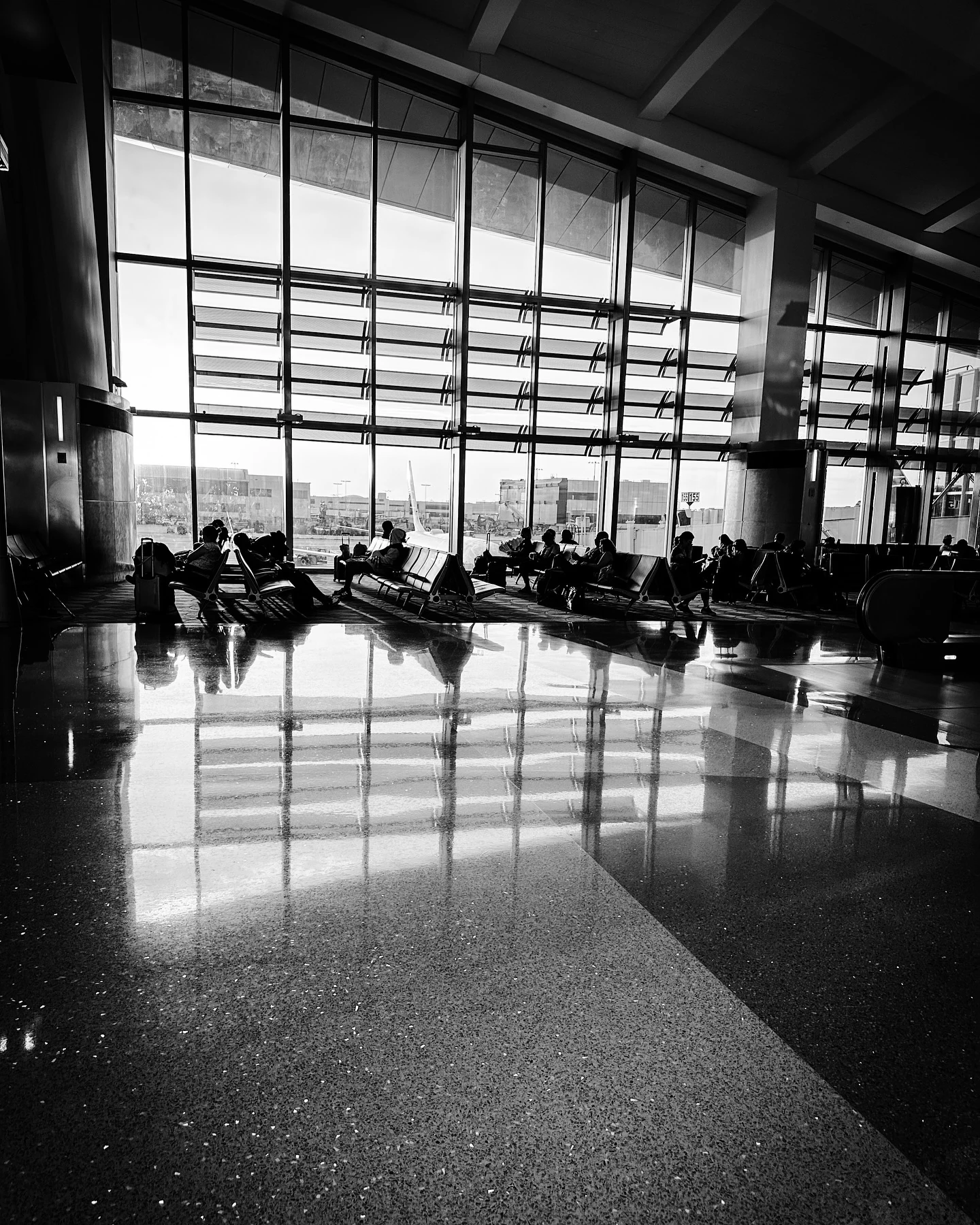 Passengers waiting by the windows at an airport departure gate