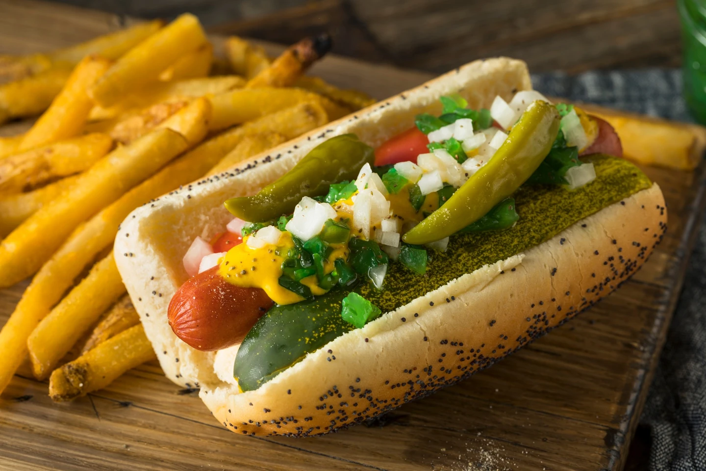 Chicago-style hot dog with mustard, relish, onion, tomato, pickle, and sport peppers on a poppy-seed bun