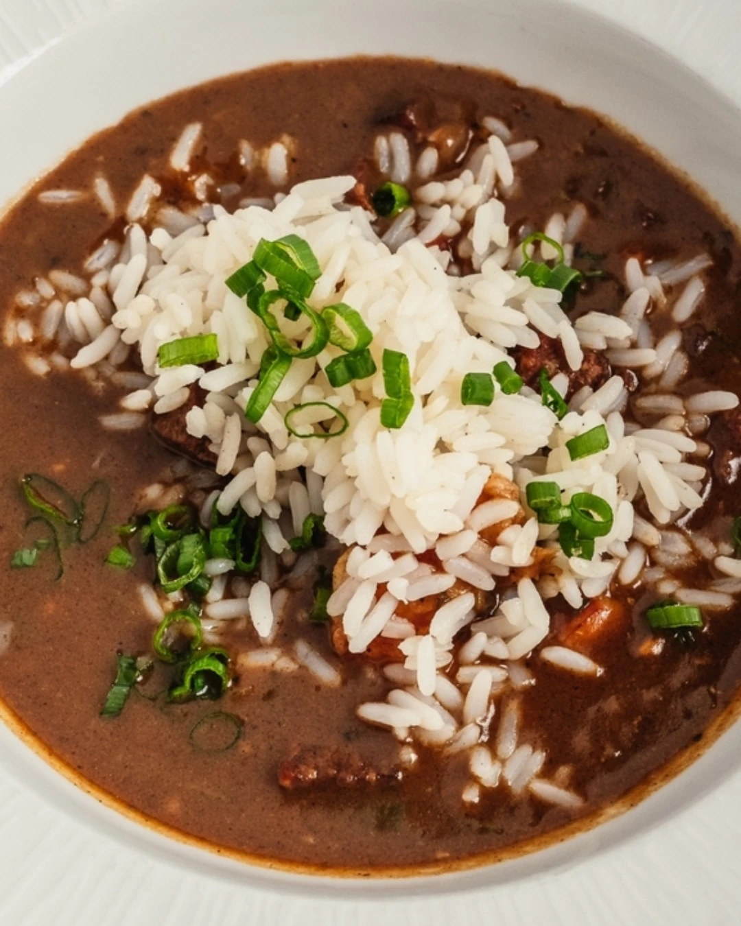 Bowl of dark-roux gumbo topped with white rice and sliced green onion