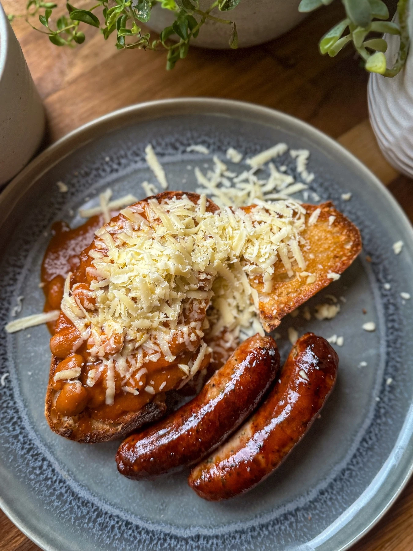 Beans in tomato sauce on toast, shown with grated cheese and sausages