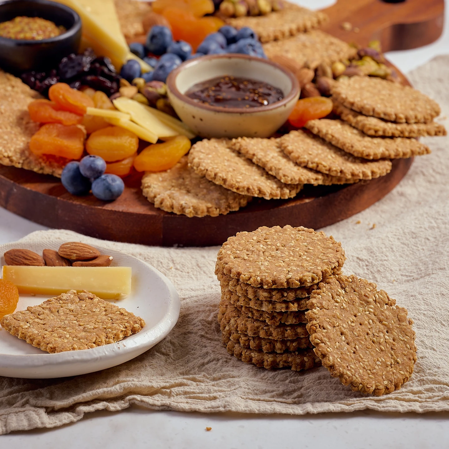 Sesame wheat crackers beside cheese, fruit and nuts