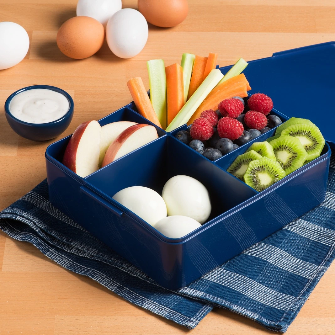 Peeled hard-boiled eggs packed in a blue bento box with fruit and vegetables
