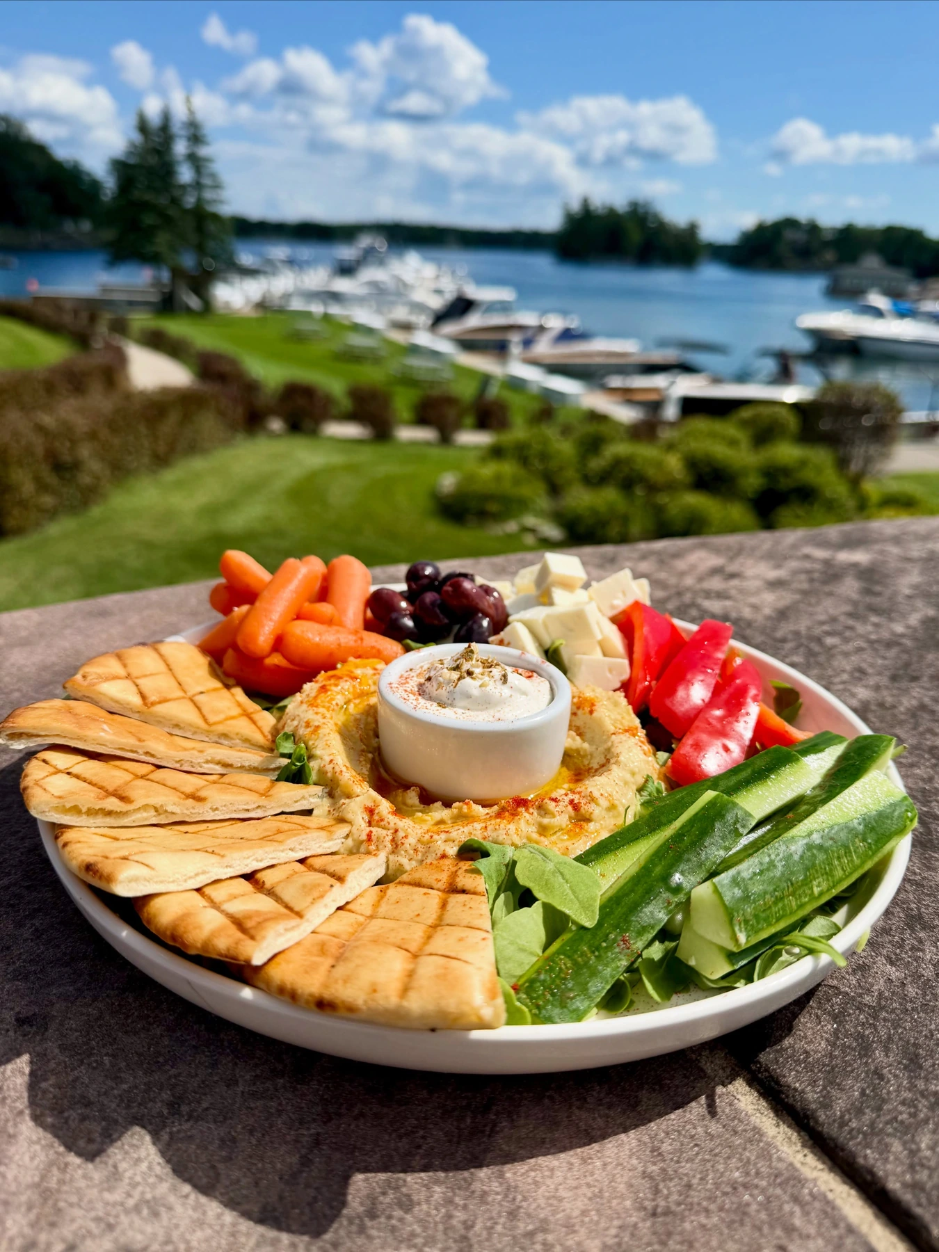 Hummus platter with cucumber sticks, carrots and red peppers beside a waterfront
