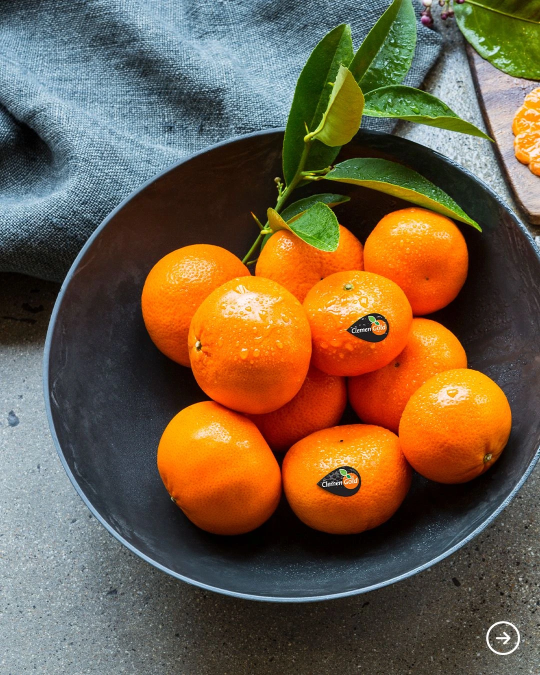 Whole mandarins with green leaves in a dark bowl