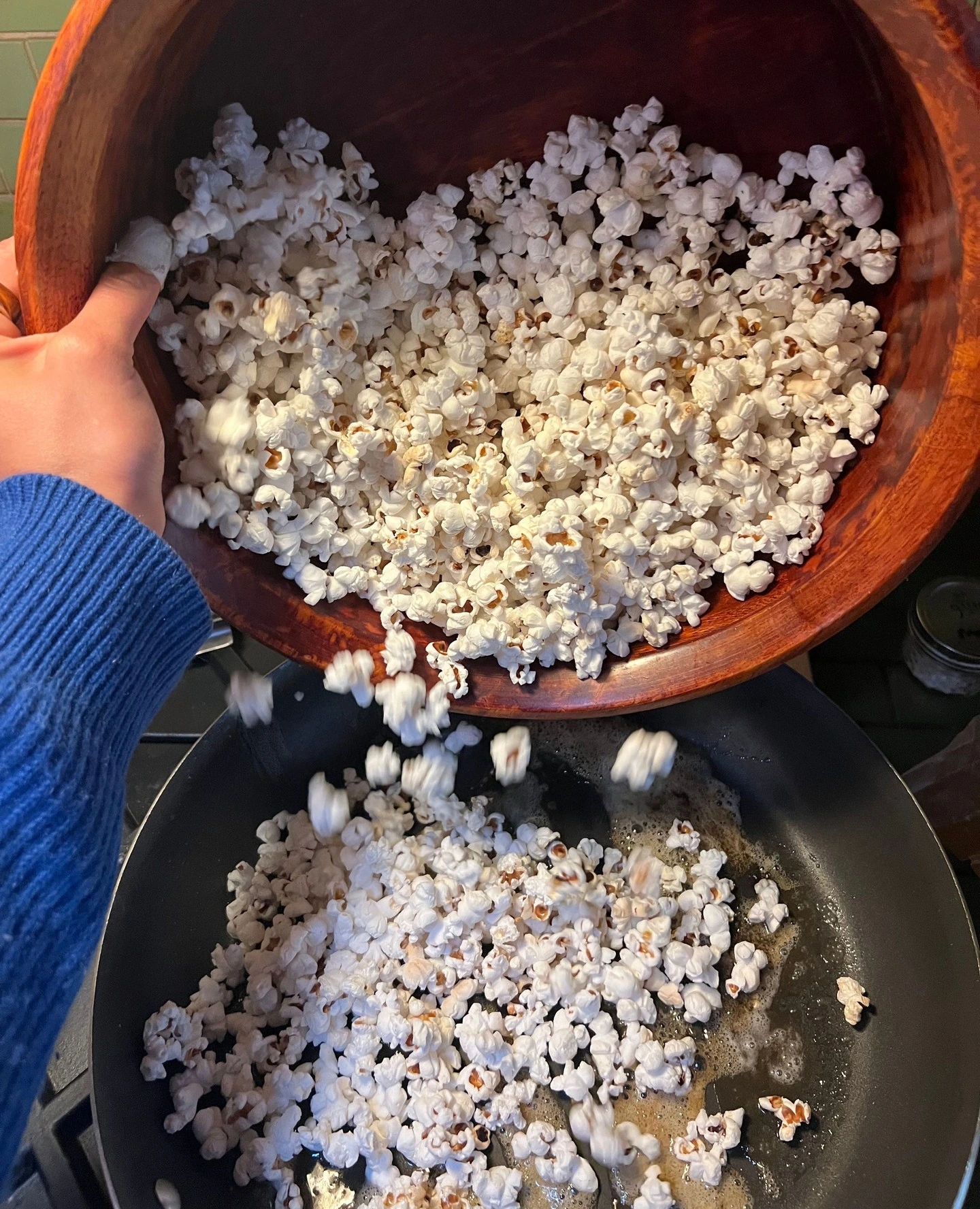 Fresh popcorn poured from a wooden bowl into a pan
