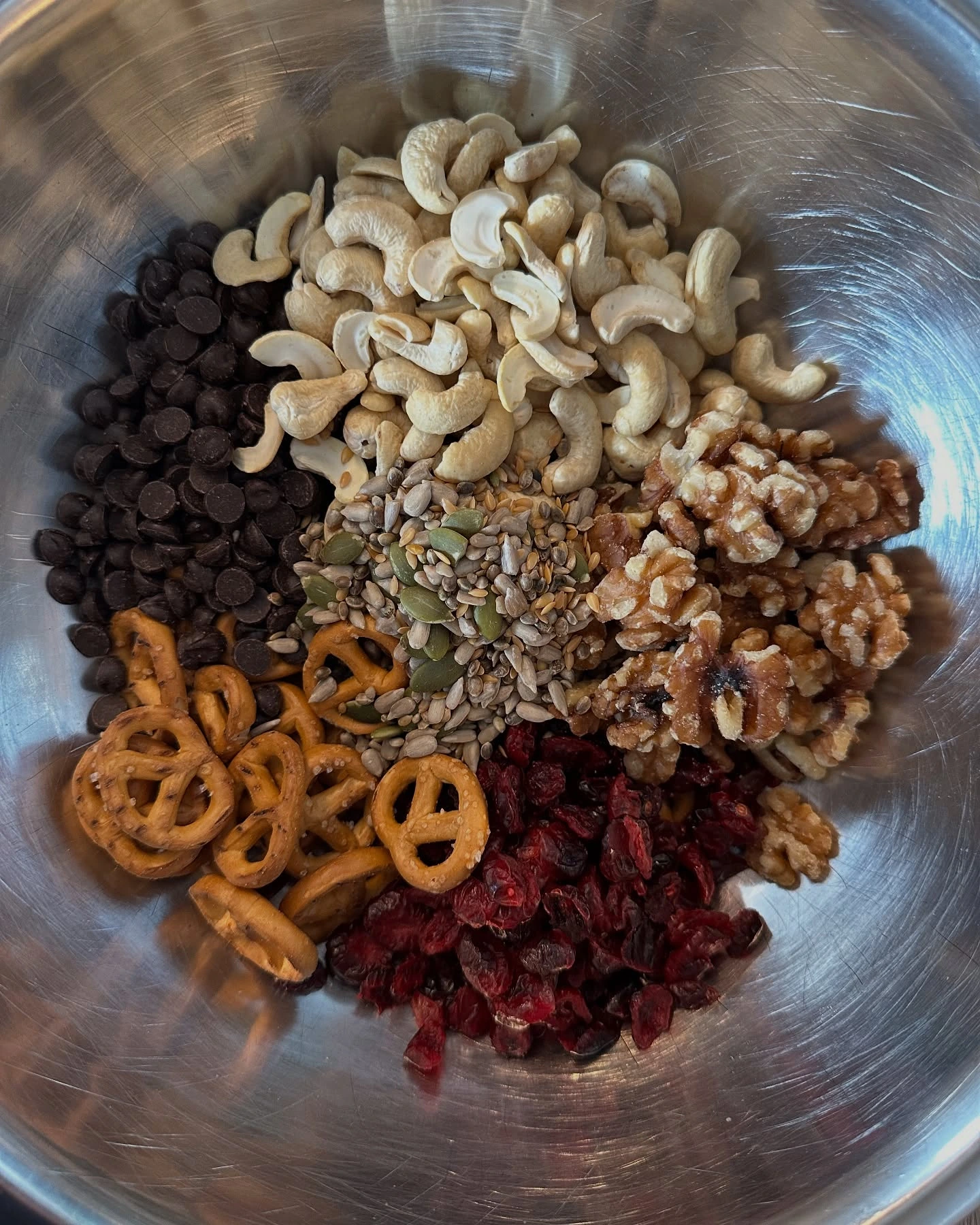 Trail mix ingredients with cashews, walnuts, seeds, dried cherries, pretzels and chocolate chips