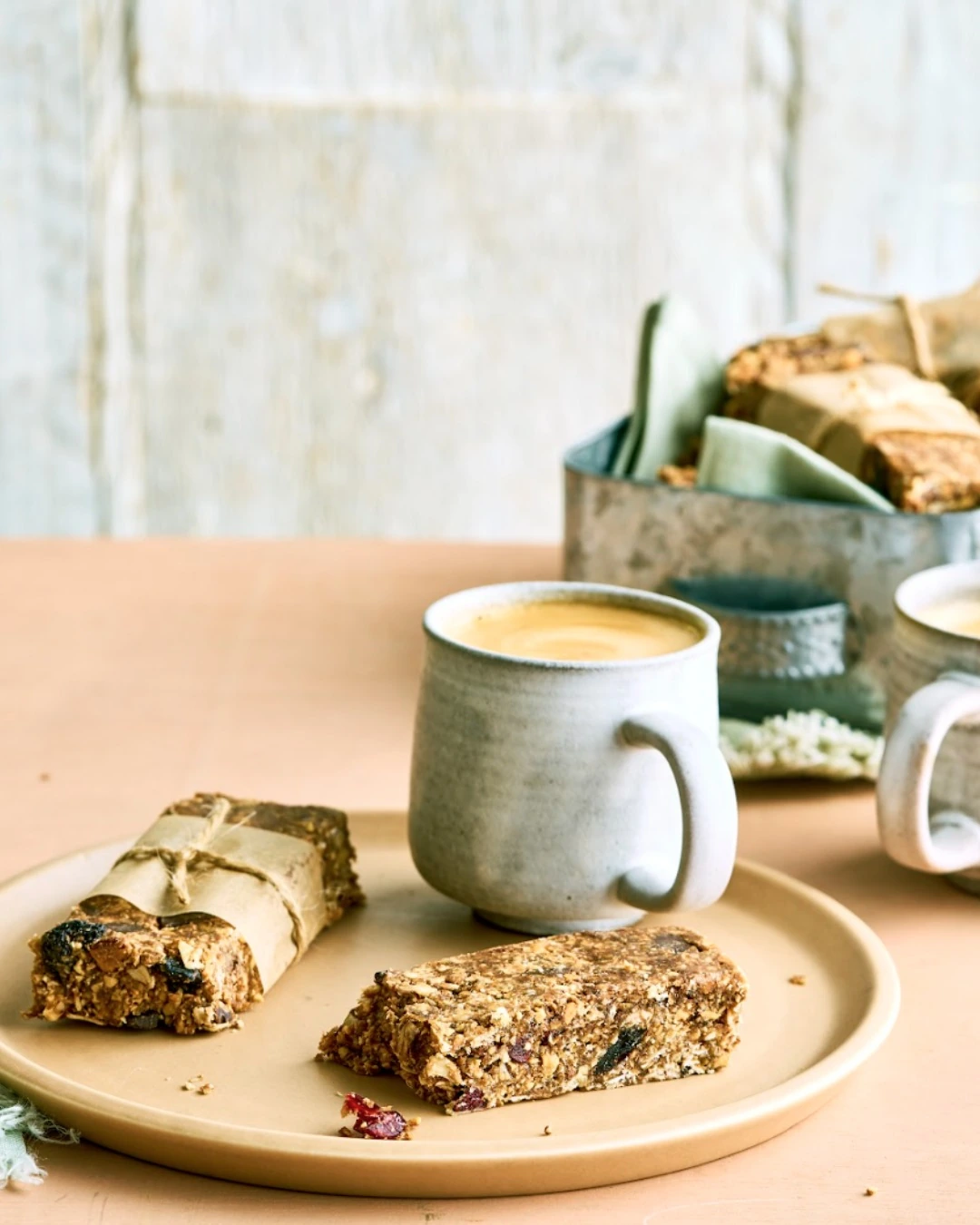 Granola bars wrapped in parchment beside an unwrapped bar and a mug